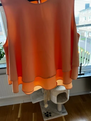 Persikofärgad ärmlös topp från Zara - Säljer en persikofärgad ärmlös topp från Zara Basic i storlek M. Toppen har dubbla lager med vågiga kanter och en rund halsringning. Materialet är lätt och känns som polyester, perfekt för varma dagar. Stängs med en liten knapp i nacken.