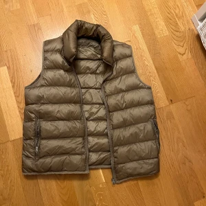 Beige dunväst från Ten c, storlek 52 - Säljer en beige dunväst från Ten c i storlek 52 vilket är M/L. Västen har quiltad design, hög krage och två sidofickor med dragkedja. Materialet är mjukt och lätt, perfekt för lager-på-lager. Stängs med dragkedja framtill och har en clean, stilren look. Ska även nämna att den har en liten fläck på framsidan (bild 3). De är inte riktigt något man tänker på om man inte kollar från nära håll.