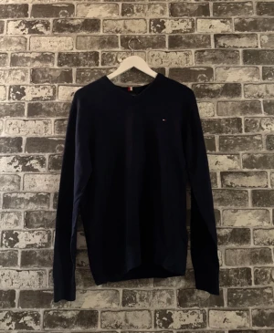 Mörkblå tröja från Tommy Hilfiger - Mörkblå långärmad tröja från Tommy Hilfiger i en mjuk mix av pima bomull och kashmir. Klassisk v-ringning och liten broderad logga på bröstet. Perfekt för dig som gillar stilrena och bekväma plagg.