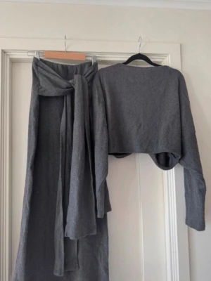 Grå croppad omlottkofta från Boohoo - Säljer en grå croppad omlottkofta från Boohoo med lång ärm och loose passform. Koftan har en snygg omlottdetalj framtill och är tillverkad i mjukt stickat material. Tillkommer en stickad kjol