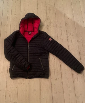 Mörkblå Colmar pufferjacka med huva - Säljer en mörkblå pufferjacka från Colmar med röd insida och huva. Storlek 12 (154-160cm) 750kr kontakta vid frågor.