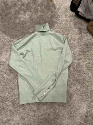 Ljusgrön polotröja Me & Lina S/M - Supersnygg ljusgrön polotröja från Me & Lina Collection i storlek S/M. Tröjan har långa ärmar och coola guldfärgade knappar vid ärmsluten. Mjuk och skön stickad känsla, perfekt för lager-på-lager under hösten och vintern.