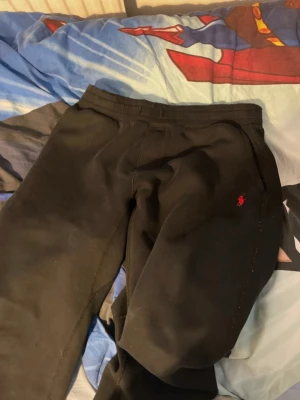 Svarta mjukisbyxor från Polo Ralph Lauren - Svarta mjukisbyxor från Polo Ralph Lauren med klassisk röd logga broderad på benet. Byxorna har elastisk midja och är gjorda i mjukt bomullsmaterial för skön passform. Perfekta för chill eller häng med kompisar.