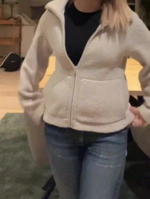 Beige teddyjacka med dragkedja - Mysig beige teddyjacka med krage och hel dragkedja framtill. Jackan har två stora fickor och är tillverkad i fluffigt fleece-material. Passformen är normal och ärmarna är långa, perfekt för att hålla sig varm under kyliga dagar. Inga synliga defekter 