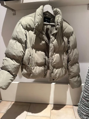 Grön pufferjacka från FB Sister XL - Säljer en grön  pufferjacka från FB Sister i storlek XL. Jackan har en hög krage, dragkedja och tryckknappar framtill samt två fickor med knappstängning. Den är quiltad och har en loose passform som ger en chill vibe. Perfekt för kalla dagar.