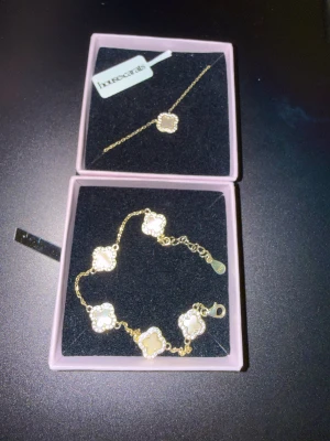 Guldig Azelia Clover set från House of Carats - Säljer en elegant guldig set från House of Carats med clover-detaljer i vit pärlemor och gnistrande stenar runt varje fyrklöver. Pärlorna är mother of pearl, är märkt med S925 och är guldpläterad med 18k finnish. Armbandet har en sten som har ramlat som knappt syns i bild (som ni ser) och i verkligheten annars är det nytt skick på båda. Köparen får en present på köpet 💕