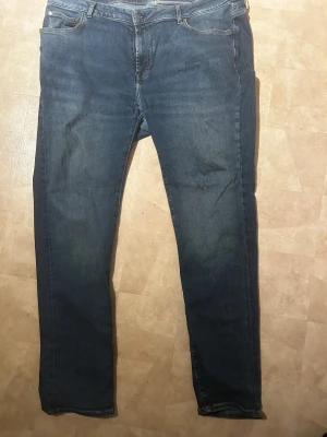 Blå jeans Dressmann Tailored Fit - Snygga blå jeans från Dressmann i modellen Tailored Fit. Klassisk femficksdesign med raka ben och normal passform. Jeansen har gul kontrastsöm och är tillverkade i slitstarkt bomullsmaterial. Perfekt för dig som gillar stilrena och tidlösa jeans.