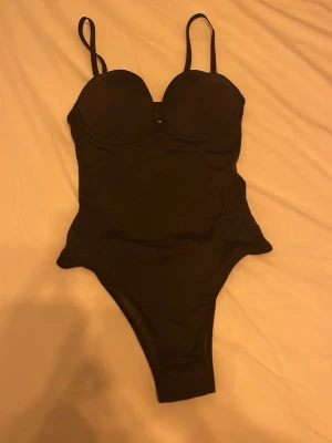 Svart body - Snygg svart body justerbara axelband. Klassisk och enkel design som ger en stilren look på stranden eller vid poolen. Hög skärning vid benen för en modern siluett.