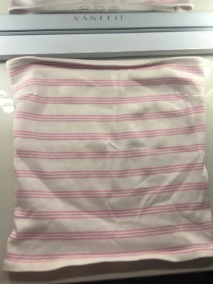 Randig bandeau tubtopp Gina Tricot - Säljer en söt bandeau tubtopp från Gina Tricot i storlek S. Toppen är vit med tunna rosa ränder och har en ribbad struktur. På insidan finns det ”gummiband” som sitter fast på insidan av tröjan så att den hålls upp ❤️ använd en gång 
