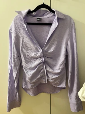 Ljuslila blus med knappar Gina Tricot - Supersnygg ljuslila blus från Gina Tricot i storlek M. Blusen har långa ärmar och krage. Materialet är lätt och har en lite skrynklig struktur. 