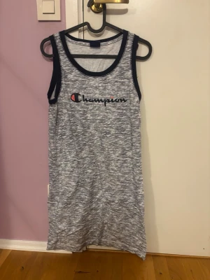 Randig ärmlös klänning från Champion - Superskön ärmlös klänning från Champion i vitt och marinblått med tunna ränder och logga framtill. Mjuk bomullskänsla och sportig look, perfekt för chill dagar. Rund halsringning och kontrastfärgade kanter.