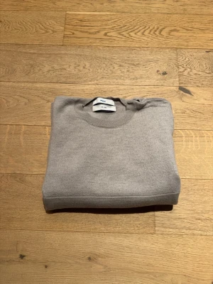 Tröja från Whyred i merinoull - Mycket fin tröja från Whyred, i stl herr S. (Det står large på etiketten, men den är vuxen herr-Small.) Den är i merino och med en fin krage med knappar. Den är så gott som ny, men med en liten (nästan osynlig) lagning i ryggen (pga fastnade i en galge). Färgen är ljus beige-grå. Mått: 52 över bröstet och 52 från halsen nedåt.