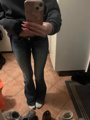 Blå x-tra low cut bootcut jeans - Säljer ett par blå jeans med extra låg midja och bootcut-ben. Jeansen har slitna detaljer, råa kanter upptill och nertill samt stora bakfickor med coola sömmar. Använda endast två gånger och kommer inte till användning då de är för små, strl xs från gina 14+