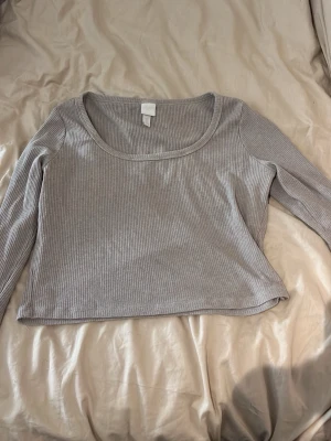 Ljusgrå ribbad långärmad topp - Säljer en beige  ribbad långärmad topp från H&M. Toppen har en croppad passform och rundad urringning. Perfekt att styla med höga jeans eller kjol för en enkel och clean look.