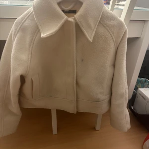 Beige teddyjacka från Gina Tricot - Supermysig beige teddyjacka från Gina Tricot med stor krage och raka ärmar. Jackan har en croppad passform och två fickor framtill. Perfekt för att hålla sig varm och snygg. En liten fläck där fram men inte orkat tvätta den då jag inte använder den. 