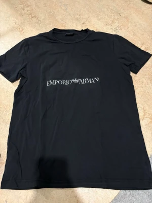 Svart EA7 Emporio Armani t-shirt - Snygg svart t-shirt från EA7 Emporio Armani med klassisk logga tryckt framtill. T-shirten har rund hals och korta ärmar, perfekt för en clean och stilren look. Tillverkad i mjuk bomull som känns skön mot huden.