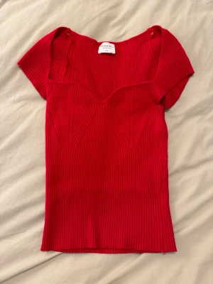 Röd ribbad offshoulder topp - Säljer en snygg röd ribbad topp från Van Der Rock. Modellen är offshoulder med korta ärmar och har en markerad byst och figurnära passform. Materialet är stretchigt och bekvämt, perfekt för att lyfta din outfit med en pop av färg.