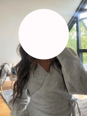 Ljusgrå omlottkofta med knytband - Supermysig mjuk ljusgrå omlottkofta och knytband i midjan. Koftan har lång ärm och är stickad i mjukt material, ganska stretchig.