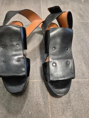 &Other Stories 36 - Svarta lädersandaler med klack - Unika svarta sandaler från & Other Stories i äkta läder. Skorna har breda remmar, fyrkantig tå och hög klack med plattform. Snygg och edgy design med nitar på ovandelen och öppen häl. Perfekta för dig som vill sticka ut!