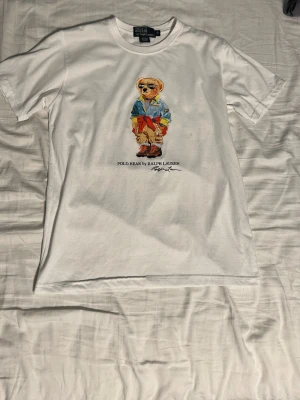 Vit ralph Lauren tröja - Säljer nu denna riktigt fräscha och stilrena polo ralph lauren t-shirt i storlek M, den har ett motiv i mitten fram med den ikoniska ralph lauren björnen på. Skriv gärna till mig om ni har några funderingar om den🙌🍾🌟