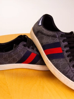 gucci ace - Säljer ett par svarta Gucci ace med klassiskt GG-mönster och ikoniska röd-blå ränder på sidan. Skorna har svarta snören, vit sula och är tillverkade i canvas med detaljer i skinn. Perfekta för dig som vill ha en lyxig och stilren look. Kommer med digitala kvitto och box 