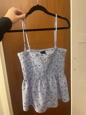 Blommig ljusblå smockad linnetopp - Supersöt ljusblå linnetopp från Gina med smockad överdel och små vita och mörkblå blommor. Toppen har tunna axelband som går att ta av för att bära som tubtopp. Luftig och perfekt för varma dagar. Den är även jättefin som kjol!!🩷 Endast använd 2 gånger så väldigt bra skick💕