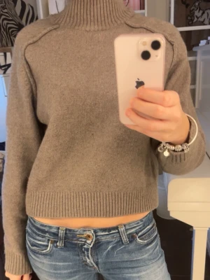 Beige/grå stickad polotröja - Mysig beige stickad polotröja med ribbad hög krage och muddar.