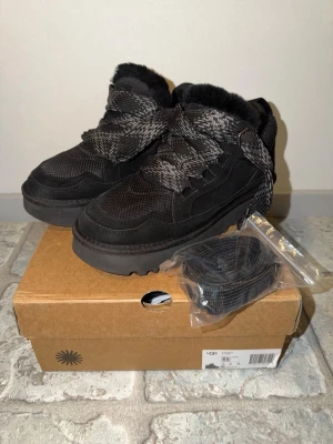 Svarta UGG Lowmell sneakers - Helt nya UGG sneakers i helsvart mocka och mesh med tjocka, mönstrade snören och fluffigt fårfoder runt öppningen. Grov sula för extra grepp och komfort. Perfekta för kyliga dagar och har en chunky, modern look. Extra skosnören medföljer. Skorna är provade inomhus men aldrig använda utomhus eller nersmutsade, säljer de då de var för små för mig. Allt i bild medföljer, priset går att diskutera vid en snabb affär. 