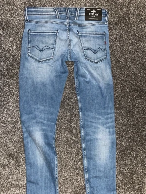Replay ljusblå slim jeans - Säljer ett par ljusblå Replay jeans med snygg tvätt och klassiska fem fickor. Jeansen har slim passform, normal midja och raka ben. Materialet är mjukt jeans-tyg i bomull med lite stretch för extra komfort. Snygga detaljer på bakfickorna och Replay-logga på linningen.