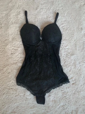 Svart spetsbody från H&M - Säljer en svart body från H&M med vadderade kupor och justerbara axelband. Bodyn har fina spetsdetaljer framtill och längs kanterna, vilket ger en snygg och feminin look. Perfekt att styla under en kavaj eller till jeans.