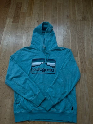 Patagonia Hoodie - Ljusblå - Perfekt skick - Den här tröjan är en ljusblå Patagonia-hoodie med en klassisk logotyp på bröstet. Den har en huva med dragsko, en känguruficka och ribbstickade muddar och nederkant. Den är i gott skick och skulle vara perfekt för utomhusaktiviteter eller bara för att slappa.