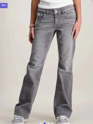 Grå bootcut jeans Gina Tricot - Säljer ett par gråa bootcut jeans från Gina Tricot med snygga broderade detaljer på bakfickorna. Jeansen har låg midja.