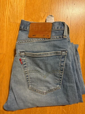 Levi's 501 ljusblå jeans W27 L28 - Klassiska Levi's 501 jeans i ljusblå tvätt med raka ben och femficksmodell. Jeansen har den ikoniska läderpatchen bak i midjan och röda Levi's-taggen på bakfickan. Tillverkade i slitstarkt bomullsjeansmaterial och har knappgylf.