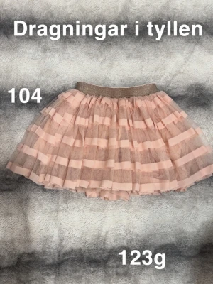 Rosa tyllkjol med glitterresår - Supersöt rosa kortkjol i tyll med breda horisontella ränder och glittrig resår i midjan. Kjolen har en fluffig volanglook och passar perfekt för dig som gillar en lekfull och trendig stil.🌸 Dragningar i tyllen ( som det blir direkt) storlek 104 