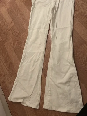Vita bootcut byxor med utsvängda ben - Säljer ett par vita byxor med riktigt utsvängda ben och bootcut-modell. De har klassisk femficksdesign och är sydda i ett mjukt bomullstyg. Perfekta för dig som vill ha en retro och clean look.
