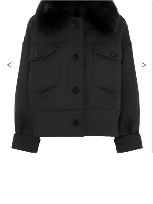 Svart kappa från Meotine  - Säljer en svart kappa från Meotine med stor fluffig krage i päls. Jackan har två stora bröstfickor med knappar, markerad midja och långa ärmar med uppvik. Stängs med knappar framtill och har en clean, snygg look.