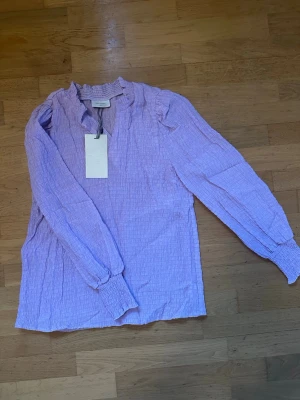 Ny lila blus  - Ny blus från Free/Quent. Super fin blus i den perfekta lila nyansen. Super fin modell med fina puffärmar som formar axeln och armen fint. Helt ny. Storlek S