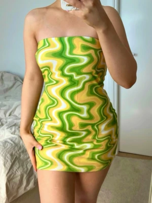 Grön och gul tubklänning med vågmönster - Supersnygg kort bandeau klänning från NA-KD, storlek XS. Stretchigt material och har ett tjockt resårband upptill så den ej ska åka ner. Fint skick 💚