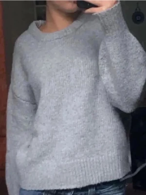 Grå stickad tröja med rund hals - Mysig grå stickad tröja med rund halsringning och ribbade muddar. Tröjan har en loose passform och långa ärmar, perfekt för lager-på-lager under kyliga dagar. Har jätte få små rosa fläckar vid halsringningen skriv privat för bilder osv