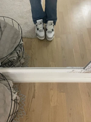 Nike Air Jordan 4 vit och grå - Säljer ett par Nike Air Jordan 4 sneakers i vitt och grått med svarta detaljer. Skorna har klassisk mesh på sidorna, perforerad tå och synlig Air-sula. Tillverkade i skinn och mocka med snörning och ikonisk Jumpman-logga på plösen. Har aldrig använts 