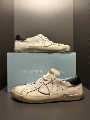 Philippe Model vita sneakers  - Snygga vita sneakers från Philippe Model med svarta detaljer på hälen och klassisk snörning. Strl 44. Skorna är tillverkade i skinn och har en beige sula samt rund tå. Perfekta för dig som gillar en stilren och trendig look. Skorna ha två slitningar under därav priset. Bara att höra av sig vid frågor!