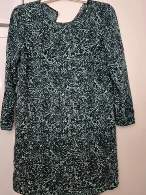 Klänning - Säljer en blå och vit mönstrad klänning från Jacqueline de Yong i storlek 38. Klänningen har lång ärm, v-ringning och ett coolt abstrakt mönster. Perfekt för dig som gillar en avslappnad men ändå snygg stil.