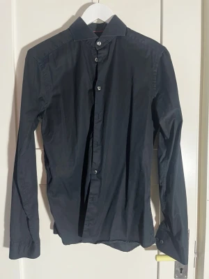 Mörkblå super slim skjorta från Eton - Snygg mörkblå skjorta från Eton i super slim passform. Klassisk krage, långa ärmar och knappar framtill. Tillverkad i mjuk bomull som känns skön mot huden. Perfekt för dig som gillar en stilren och tajt look.