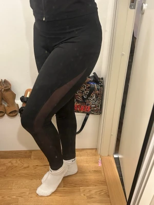 Svarta träningstights Adidas Stella McCartney - Svarta träningstights från Adidas, designade i samarbete med Stella McCartney. Gjorda i Climalite-material som andas och transporterar bort fukt. Snygga sömdetaljer och stretchig material. Meshdetaljer längst sidan av benen.