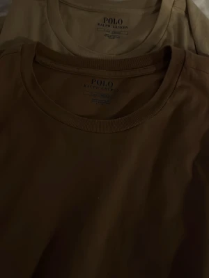 Beige och brun t-shirt Polo Ralph Lauren - Två stilrena t-shirts från Polo Ralph Lauren i beige och brun färg. Klassisk rund halsringning och korta ärmar. Perfekta basplagg i mjuk bomull som funkar till allt. Diskret logga i nacken för clean look.