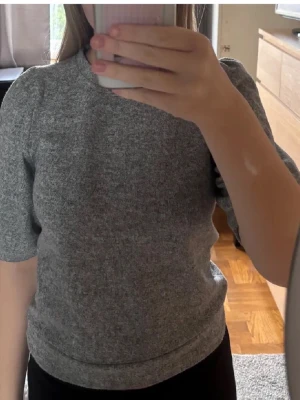 Grå puffärmstickad tröja 157 S - Mysig grå stickad tröja från 157 i storlek S. Tröjan har puffiga korta ärmar och en rund halsringning. Perfekt till höst och vinter när du vill ha något enkelt men ändå snyggt. Passformen är normal och materialet känns mjukt och bekvämt.