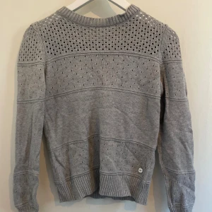 Ljusgrå stickad tröja från 365 - Superfin ljusgrå stickad tröja från 365 med hålmönster och ribbade muddar. Tröjan har rund halsringning och långa ärmar, perfekt för lager på lager. Enkel att matcha med jeans eller kjol för en chill look.