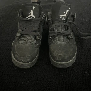 Svarta Nike Air Jordan 4 sneakers (ej äkta) - Säljer ett par helsvarta Nike Air Jordan 4 sneakers med klassisk meshpanel, coola detaljer och Jumpman-logga både fram och bak. Skorna har snörning och en chunky sula med synlig luftbubbla. Perfekta för dig som gillar streetstyle och vill sticka ut. Lite slitna och saknar en skosnöre på ena skon annars väldigt bra plagg att ha för streetwear