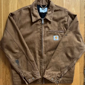 Carhartt OG Detroit Workwear Jacket - Klassisk workwear jacka från Carhartt. OG Detroit jacket, Duck Brown, storkek S. Har använts vid arbete av förra ägaren, små whiskers och färgfläckar finns. Överlag väldigt bra skick. Inga hål. Dragkedjan fungerar felfritt.  Längd: 63cm Bred (axel till axel): 48cm