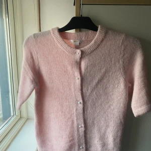 Ljusrosa kofta från Gina Tricot - Superfin ljusrosa kofta från Gina Tricot med korta ärmar och pärlknappar framtill. Koftan är stickad och har en mjuk, fluffig känsla. ger en söt touch till din outfit. ALDRIG ANVÄND!